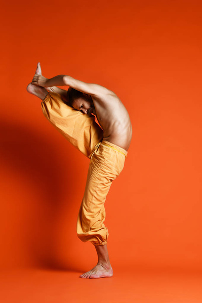 Old man practicing yoga doing stretching exercises against orange background - Fotoğraf, Görsel