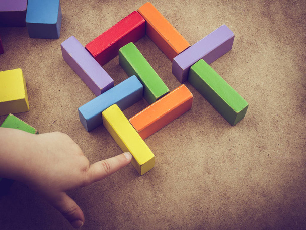 Toddler mão sobre blocos de construção coloridos no fundo marrom
 - Foto, Imagem