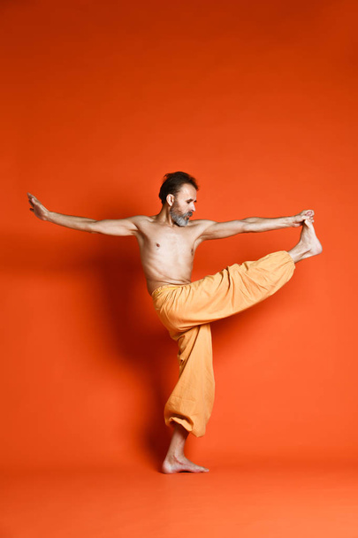  man practicing yoga doing stretching exercises against orange background - Photo, image