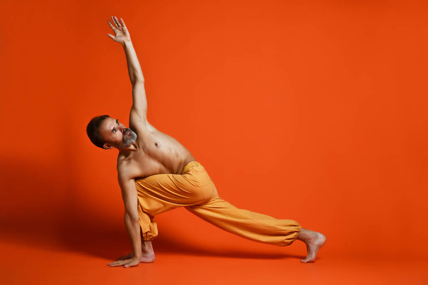 Old man practicing yoga doing stretching exercises against orange background - Valokuva, kuva