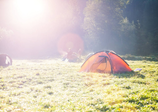 Orangefarbenes Zelt auf dem Campingplatz. Ruhe in der Natur. Zelten auf der grünen Wiese. Morgendämmerung im Wald. - Foto, Bild