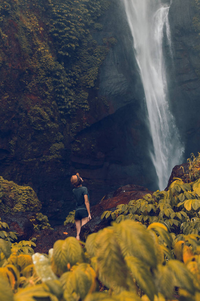 Молодая женщина позирует на большом водопаде Секумпул в глубоком тропическом лесу острова Бали, Индонезия
. - Фото, изображение