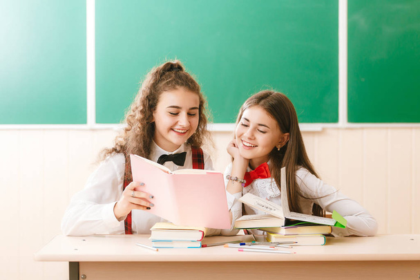 duas alunas brun.ette se sentam na sala de aula em sua mesa com livros no fundo do blackboard.girls sentar em uma lição de escola
 - Foto, Imagem