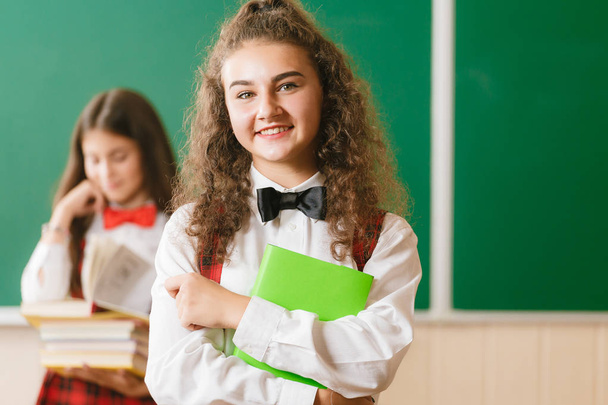 books.schoolgirl、カメラ目線と笑顔教室に立つ赤い学校の制服のブルネット女子中学生 - 写真・画像