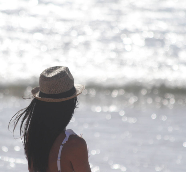 Красивая девушка, видна сзади, в шляпе, которая смотрит на море. Море на заднем плане. Сабаудия, Лацио, Италия
 - Фото, изображение