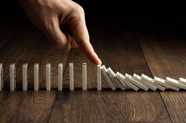 Creative background, Men's hand stopped domino effect, on a brown wooden background. Concept of domino effect, chain reaction, risk management, copy space. - Zdjęcie, obraz