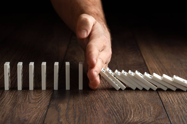 Creative background, Men's hand stopped domino effect, on a brown wooden background. Concept of domino effect, chain reaction, risk management, copy space. - Photo, Image