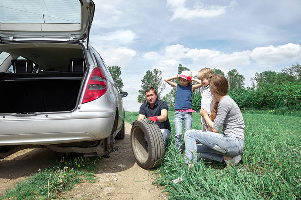 father replaces the damaged tire of the family car. - Foto, Bild