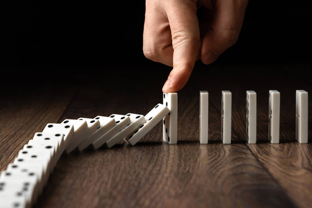 Creative background, Men's hand stopped domino effect, on a brown wooden background. Concept of domino effect, chain reaction, risk management, copy space. - Photo, image