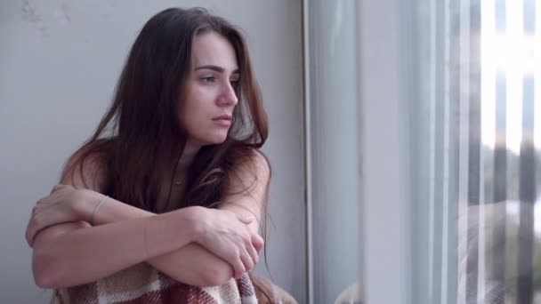 junge traurige emotionslose Frau, die auf dem Boden sitzt und direkt vor einem das Fenster anstarrt und sich deprimiert fühlt. einsame verzweifelte Frau mit Selbstmordgedanken. - Filmmaterial, Video