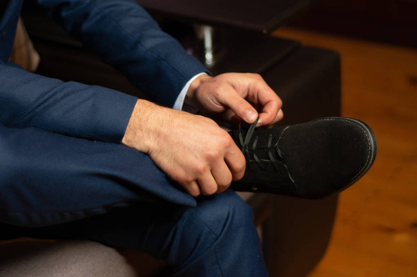 a future husband tightens up for a wedding by putting on his shoes and tying his ties. 2019 - Foto, Bild