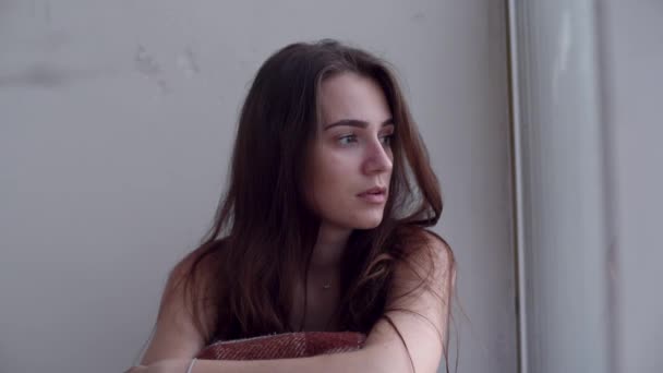 Eine junge, traurig depressive Frau sitzt auf dem Boden und schaut aus dem Fenster. einsame verzweifelte Frau mit Selbstmordgedanken. - Filmmaterial, Video