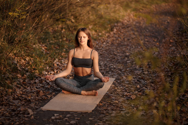 Giovane donna che pratica esercizio di yoga nel parco autunnale con foglie gialle. Stile di vita sportivo e ricreativo
. - Foto, immagini
