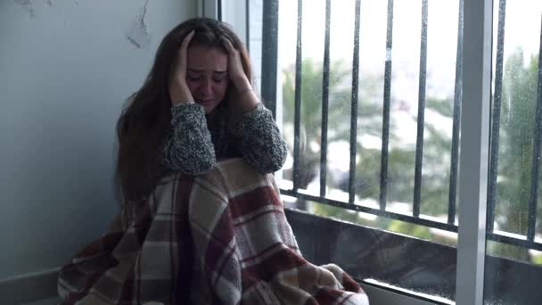 Eine depressive Frau weint auf dem Boden am Fenster sitzend, während draußen Regen fällt. einsame verzweifelte Frau mit Selbstmordgedanken. - Filmmaterial, Video