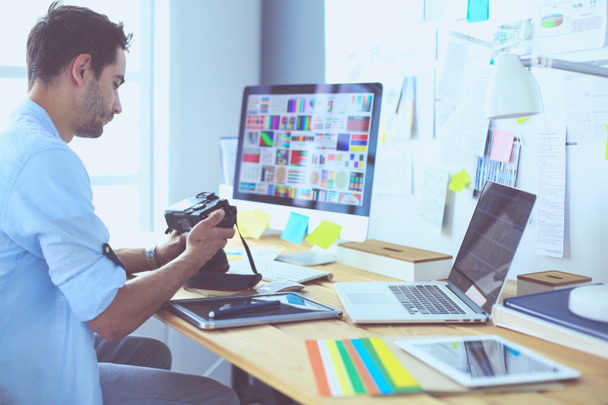 Портрет молодого дизайнера, сидящего в графической студии перед ноутбуком и компьютером во время работы в сети. - Фото, изображение