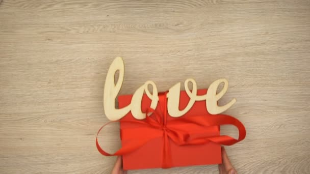 Hand putting red gift box with wooden love word on table, Valentines Day present - Felvétel, videó