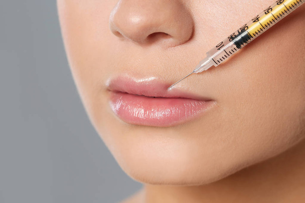 Young woman getting lips injection on grey background, closeup. Cosmetic surgery - Φωτογραφία, εικόνα