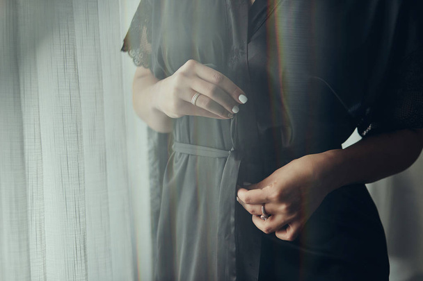 Mädchen bindet Gürtel an ihr Gewand, das am Fenster steht, Frau bereitet sich vor Hochzeitszeremonie vor - Foto, Bild