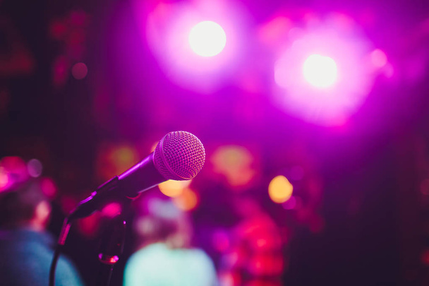 Microphone on a stand ready for live music performance or karaoke night with soft bokeh lights and people silhouettes in the background. Concept for musical singing event, having a good time. - Photo, Image
