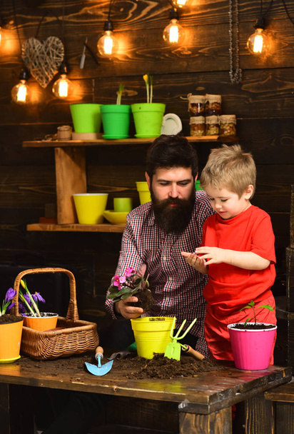 Father and son. happy gardeners with spring flowers. Flower care watering. Soil fertilizers. bearded man and little boy child love nature. Family day. Greenhouse. Enjoying their work with plants - Foto, Imagem