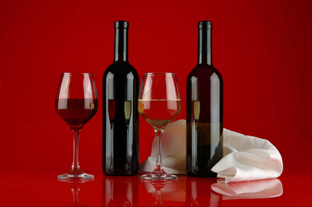 Still life with glasses and bottles of red and white wine on a glossy Burgundy background - Foto, Imagen