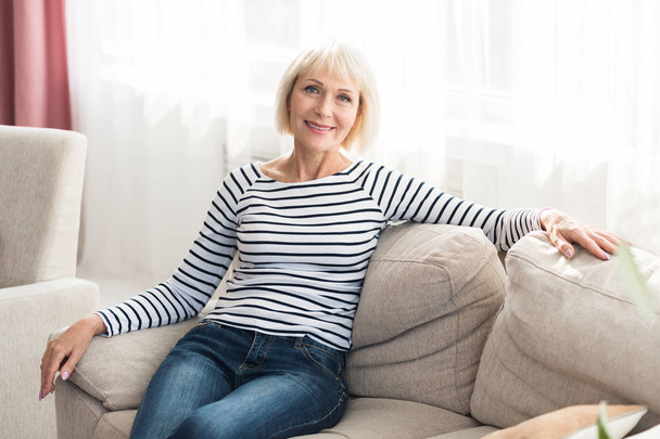 Весела старша жінка відчуває себе щасливою і розслабленою, сидячи на дивані
 - Фото, зображення