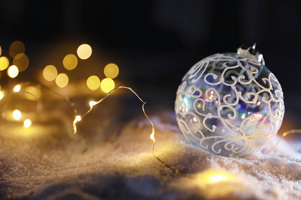 Christmas ball and fairy lights on white snow outdoors. Space for text - Photo, Image