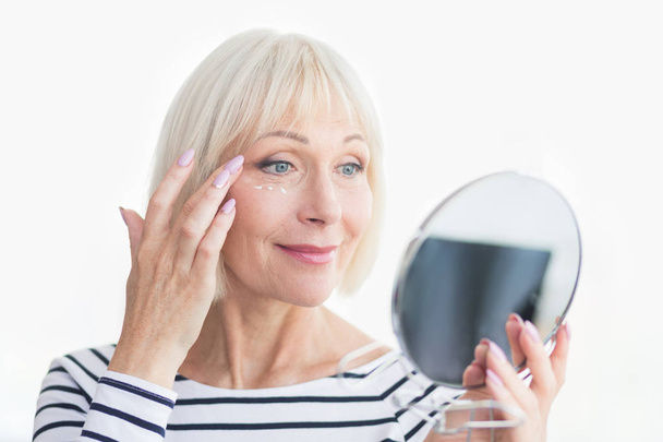 Gelukkig senior vrouw toepassen van anti-rimpel oogcrème - Foto, afbeelding