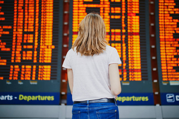 Young woman in international airport with luggage near flight information display - Φωτογραφία, εικόνα