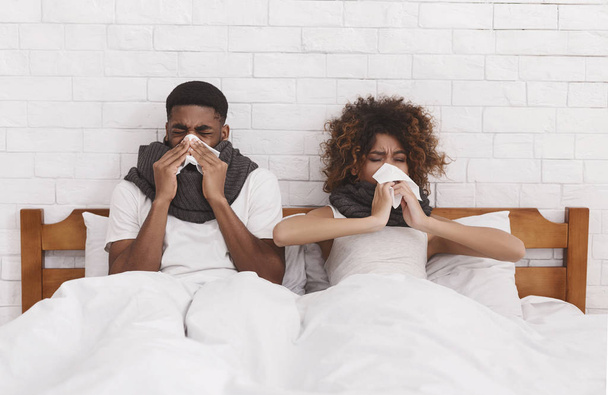 Sick african-american couple blowing noses in bed - Fotó, kép