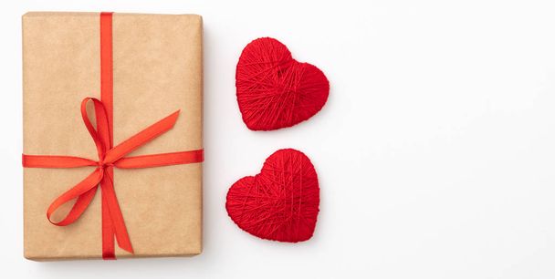 Valentine dzień ozdoba z craft papier pudełko z czerwoną wstążką i małe czerwone serca na białym tle. Widok z góry. Lay miłości dzień koncepcji płaskie - Zdjęcie, obraz