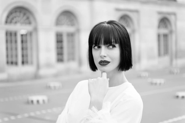 Mysterious female has idea. Girl fashionable lady with bob hairstyle outdoor urban architecture background. Woman fashionable model posing outdoor. Girl brunette bob hairstyle looks stylish - 写真・画像