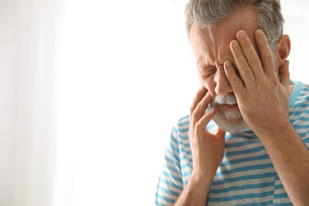 Volwassen man lijdt aan sterke tand pijn op lichte achtergrond, ruimte voor tekst - Foto, afbeelding