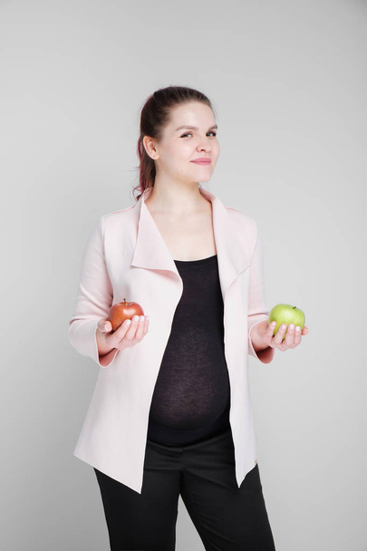 Беременная женщина держит зеленые и красные яблоки
. - Фото, изображение