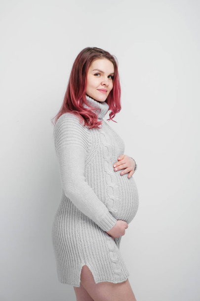 Μια έγκυος γυναίκα με χρώμα βυσσινί μαλλιών σε ένα γκρι πλεκτό πουλόβερ. - Φωτογραφία, εικόνα
