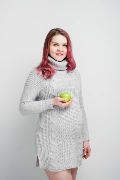 A pregnant woman is holding green and red apples. - Фото, изображение