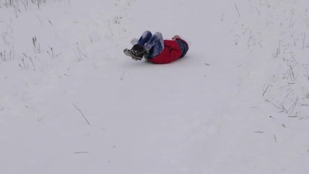vidám gyermek a piros kabát diák szán a hóban egy magas hegy és nevet. boldog lány játék karácsonyi ünnep a téli park. Lassú mozgás - Felvétel, videó