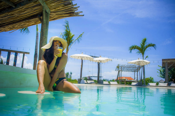 joven sexy y atractiva exótica mujer asiática en bikini y sombrero de verano beber jugo en el paraíso piscina resort bar sonriendo feliz disfrutando de vacaciones de lujo viaje en la isla tropical
 - Foto, Imagen