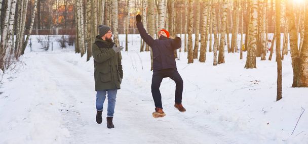 Two young modern man while walking through a birch forest in winter. One of them slipped and lost his balance, his friend held out his arms. Freeze frame before falling into the snow. - Photo, image
