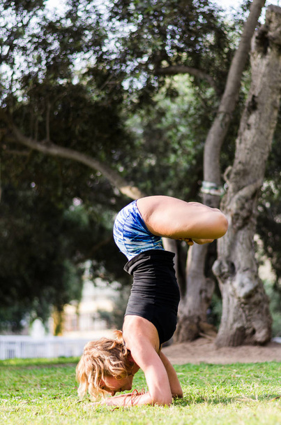 Young girl standing on her head doing yoga in the park - Foto, Imagem