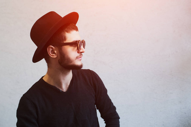Profile portrait of young bearded guy, wearing sunglasses and black hat over white background - Фото, изображение