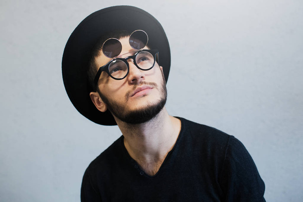 Portrait of bearded hipster guy who looking up, wearing sunglasses and black hat, over white background. - Foto, afbeelding