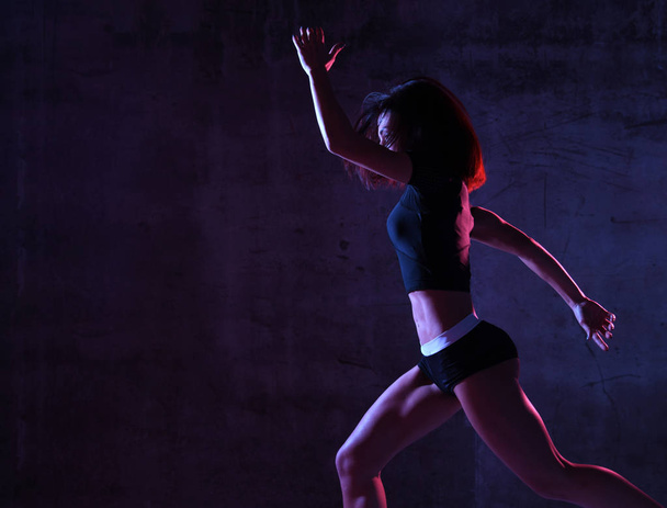 Young sport woman running jogging in gyn in blue and pink neon light on dark wall  - Fotoğraf, Görsel