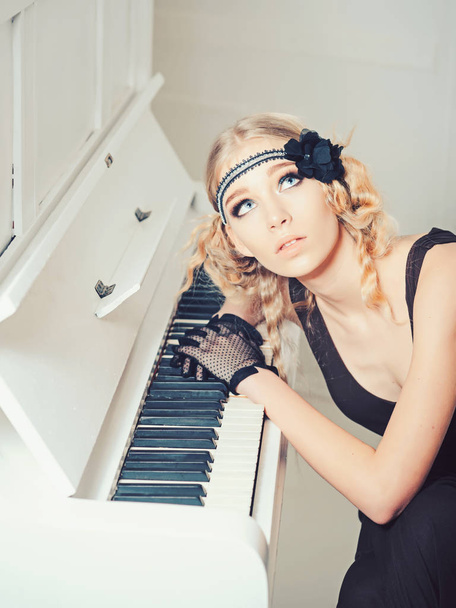 Young actress with blue eyes looking up while lying on open keyboard of white piano - 写真・画像