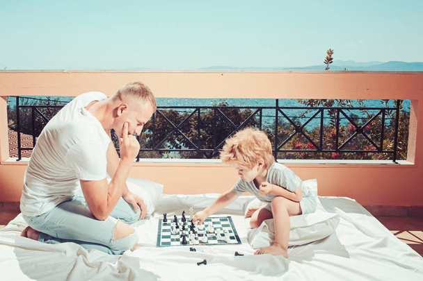 Love and trust as family values. Child play chess with father. Summer vacation of happy family. Family travel with kid on fathers day. father with son on balcony play chess - Photo, image