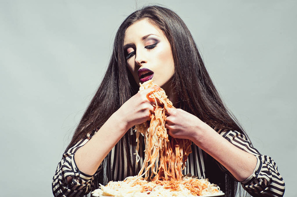 Sexy woman eat spaghetti with hands. Woman eat pasta dish with tomato ketchup. Hungry girl have italian food meal. Beauty model with makeup and long brunette hair have dinner. Food, diet and cuisine - Photo, Image