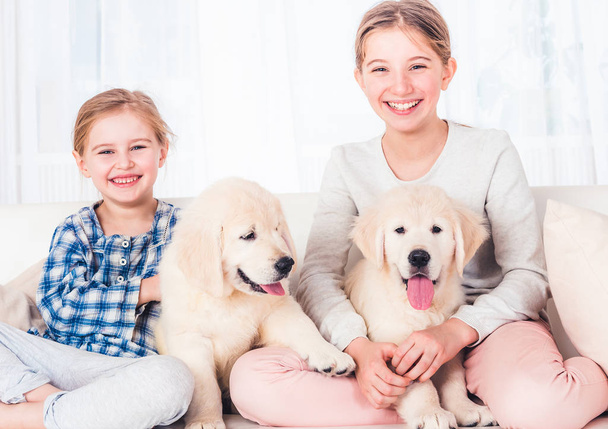 Smiling sisters sitting with cute fluffy puppies on sofa - Foto, Bild