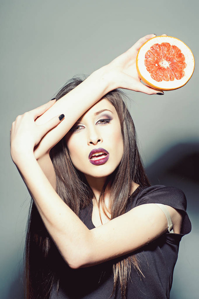 Sensual woman with grapefruit half. Woman with vitamin citrus fruit. Beauty model with makeup and long brunette hair. Food diet and health concept - Foto, afbeelding