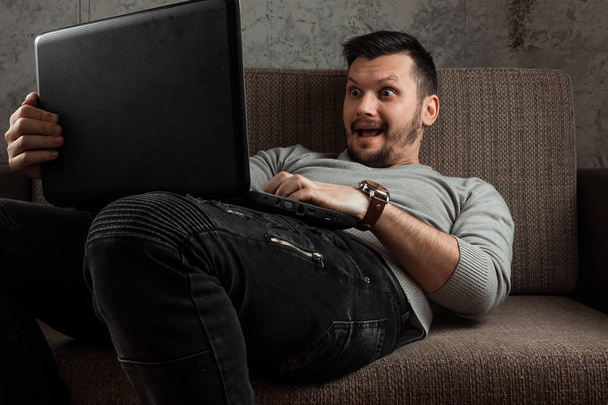 A man watches an adult video on a laptop while sitting on the couch. The concept of porn, men's needs, pervert, lust, desire, loneliness. - Valokuva, kuva