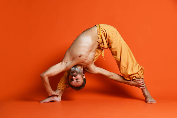 Old man practicing yoga doing stretching exercises against orange background - Fotoğraf, Görsel